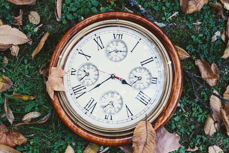 Vintage clock with Roman numerals among autumn leaves