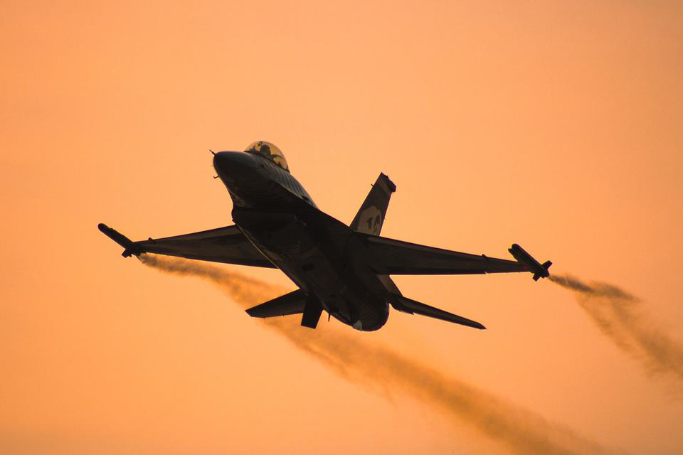 Silhouette of an F-16 aircraft against an orange sunset sky