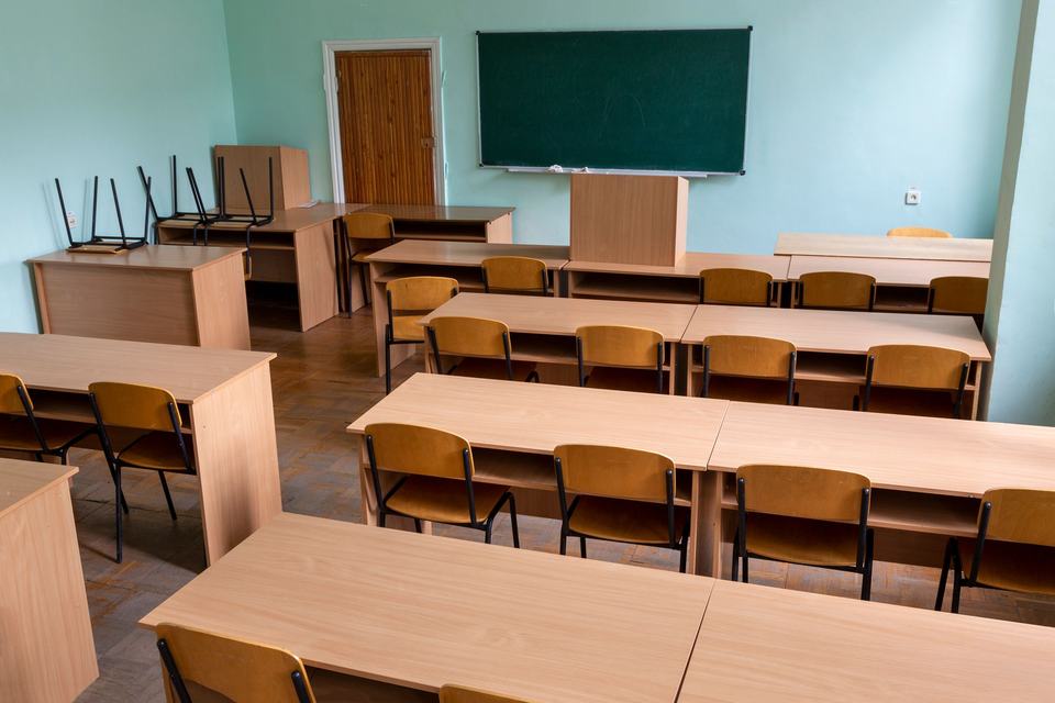 Rows of wooden desks and a green board in an empty classroom